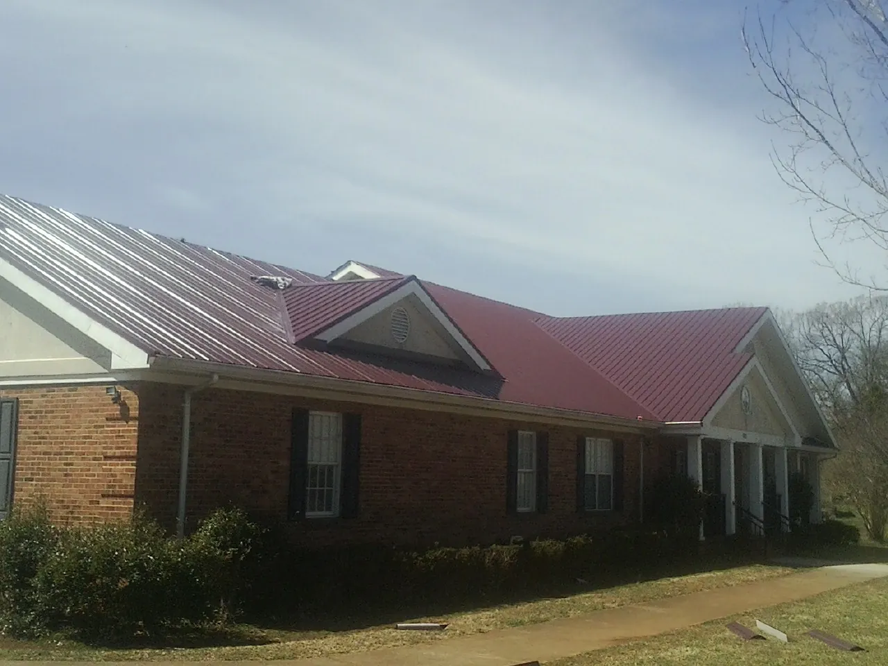 Red metal roof with gabled entries on a long brick building, from a Hail Damage Roof Repair job in Morgan Hill