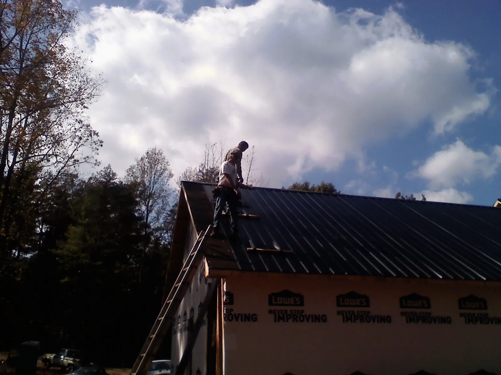 Roofer fastening dark metal panels high against a cloudy sky, from a Roof Inspection job in Morgan Hill