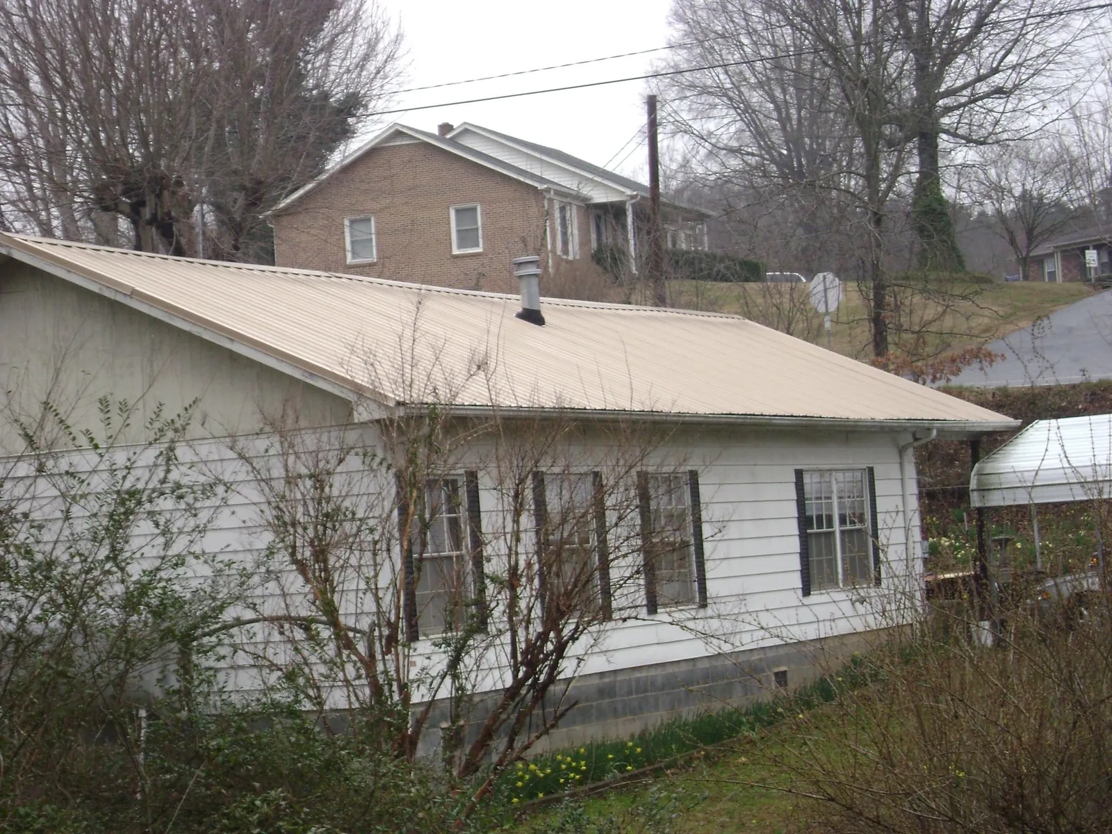 Tan metal roof on a white sided house set into a hillside — Commercial Roofing by Roofing Brothers in Morgan Hill